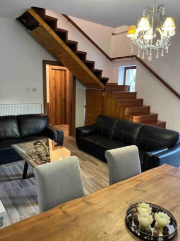 Living room with black sofas, dining table and wooden staircase in Pavliani Oiti – σαλόνι με καναπέδες και ξύλινη σκάλα στην Παύλιανη Οίτης